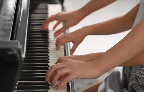 Little girl playing piano with teacher indoors, closeup Playing piano